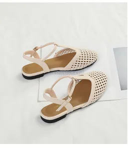 Dettaglio di sandali beige intrecciati con cinturino a T e fibbia dorata elegante.