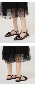 Detail view of black flat camellia sandals with open-toe Roman style and ankle buckle.