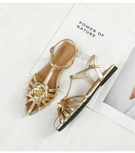 Detail of gold camellia flower flat sandals with T-strap and ankle buckle strap