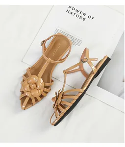 Detail view of flat sandals with camellia flower decoration and cage straps in beige