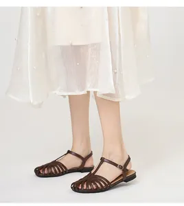 Detailed close-up showing vintage brown hollow-out T-strap flat sandals on a model outdoors