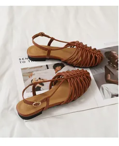 Macro view of brown handmade woven flat roman sandals featuring adjustable buckle strap