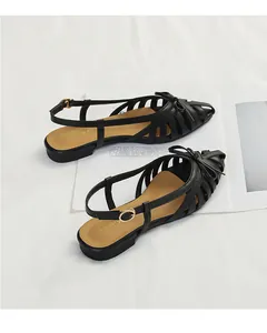 Elegant black woven hollow sandals with bow detail styled on a white fabric background.