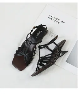Detail view of black cross-strappy sandals with a unique sculptural heel and square toe