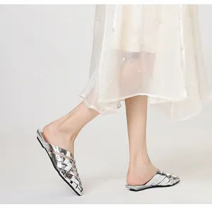 Detailed side view of silver metallic woven pointed-toe mules on model feet.
