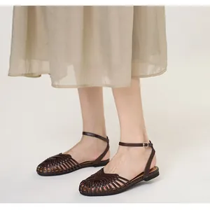 Model wearing dark brown handmade woven retro Roman sandals with an ankle strap and beige skirt.