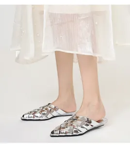 Close-up shot of silver woven pointed toe mule slippers paired with an elegant white skirt