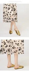 Detailed view of elegant golden woven pointed-toe mule shoes styled with a floral skirt.