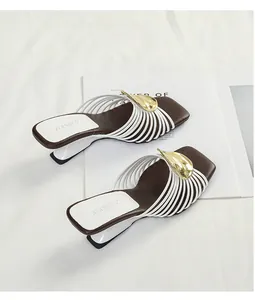 Detailed view of white multi-strap sandals with gold leaf buckle and brown footbed