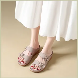 Close-up of women's beige wedge sandals featuring dual gold belt buckles and textured straps.