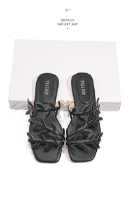 Detail view of black flat sandals featuring intricate leaf pattern straps and square toe.