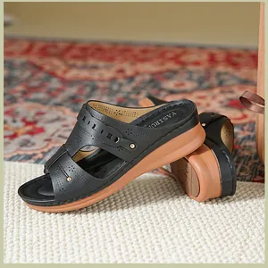 Detail view of black women's wedge sandals with laser-cut patterns on a textured rug