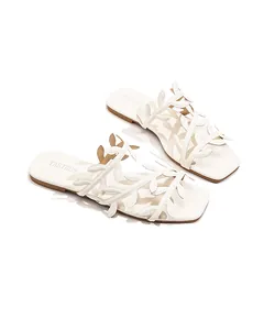 Close-up detail of white square-toe flat sandals with leaf-shaped cut-out straps