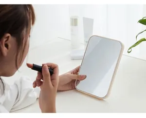 Gros plan d'une femme utilisant un miroir de maquillage pliable beige sur un bureau blanc.