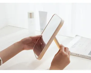 Vue de côté d'un miroir de maquillage pliable beige portable tenu par des mains