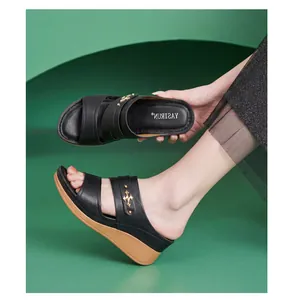 Close-up of black leather wedge sandals with gold hardware on a green background.