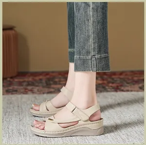 Detailed side view of beige wedge sandals with stitched patterns and denim jeans.
