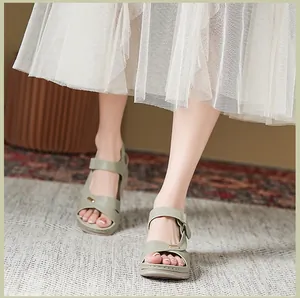 Close-up view of light green wedge sandals with stitched straps shown on model's feet