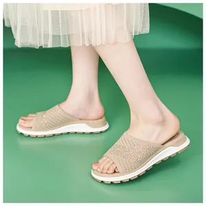 Close-up of beige fly-knit slide sandals with sparkling rhinestones on model's feet