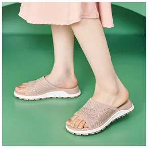 Close-up view of pink knitted flat slide sandals with sparkling rhinestones on model's feet