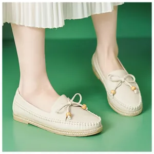 Close-up of beige leather loafers with bow and wooden beads on a green background.
