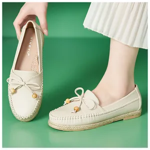 Close-up detail view of cream loafers with bow and wooden beads on a green background