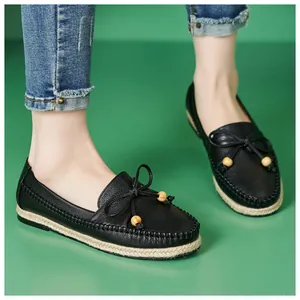 Black leather loafers for women with decorative bow and wooden beads on green background