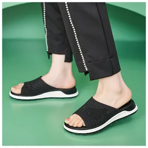 Detail view of stylish black flyknit rhinestone flat sandals worn with elegant trousers