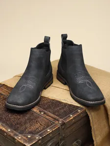 Detail view of black men's Chelsea boots with decorative white stitching on a vintage trunk