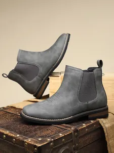 Close-up detail of grey men's Chelsea boots featuring elastic side panels in a studio setup