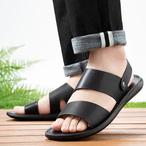 Close-up detail of black two-way men's beach sandals on a wooden deck with a fern
