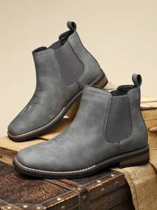Close-up of grey faux leather Chelsea boots with elastic side panels and fine stitching.