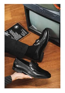 Close-up of men's black leather loafers with vintage TV background.