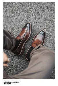 Close-up of men's brown gradient leather loafers worn on an asphalt road surface