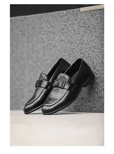 Close-up of black crocodile-embossed leather loafers leaning against stone wall