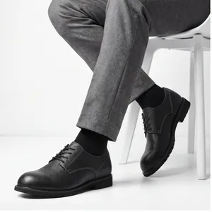 Dettaglio di scarpe derby in pelle nera martellata abbinate a eleganti pantaloni grigi