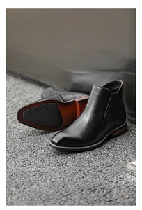Detail view of men's black leather Chelsea boots with side zipper and dual-tone sole.
