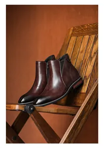 Detail of dark brown leather Chelsea boots with side zipper on a vintage wooden chair