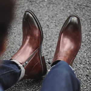 Stylish men's brown leather Chelsea boots with side zippers on asphalt ground