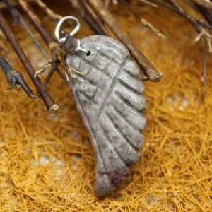 Carved wing-shaped grey natural stone pendant with silver bail on straw background