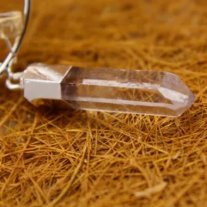 Clear white quartz crystal hexagonal point pendant displayed on a natural straw background