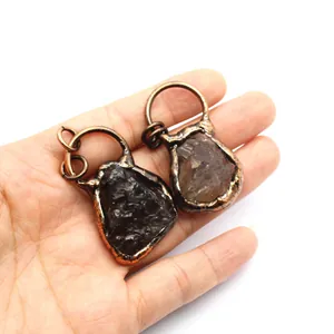 Handheld close-up showing two unique raw smoky quartz pendants with antique copper wire wrap.