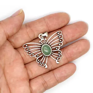 Detailed macro view of vintage butterfly pendant with green gemstone held in hand