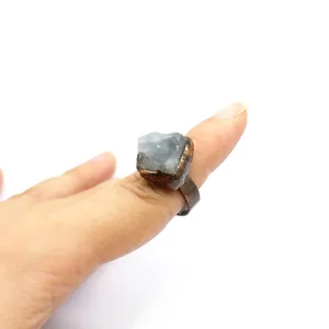 Dettaglio di un anello vintage in rame con pietra grezza di fluorite blu su un dito.