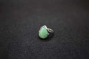 Close-up of a silver-tone ring with a teardrop-shaped green stone on black felt