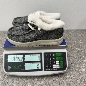 Graue Tweed-Wintermokassins mit Pelzfutter, die auf einer digitalen Waage gewogen werden.