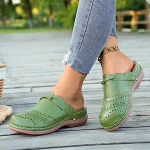 Close-up view of green retro mules with laser-cut floral patterns and white stitching