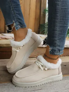 Detailed view of women's beige fur-lined snow boots with laces and rustic wood background