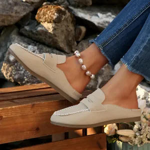 Close-up view of elegant beige suede flat loafer mules with decorative white stitching
