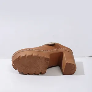 Detail view of brown chunky high-heeled clogs featuring white stitching and floral engraving